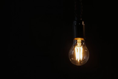 Photo of Glowing light bulb hanging on dark background. Space for text