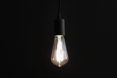 Photo of Glowing light bulb hanging on dark background