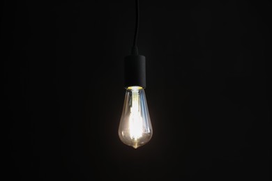 Photo of Glowing light bulb hanging on dark background