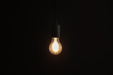 Photo of Glowing light bulb hanging on dark background