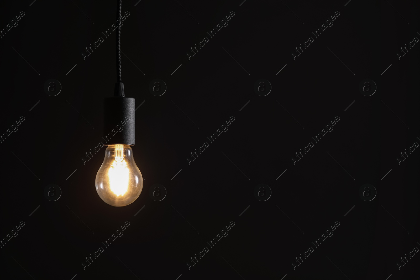 Photo of Glowing light bulb hanging on dark background. Space for text