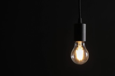 Photo of Glowing light bulb hanging on dark background. Space for text