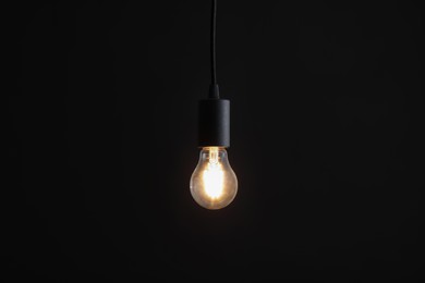 Photo of Glowing light bulb hanging on dark background