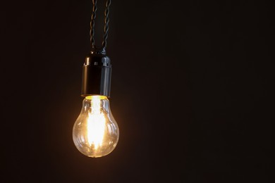 Photo of Glowing light bulb hanging on dark background. Space for text