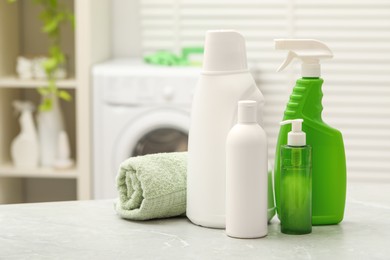 Photo of Different laundry detergents and rolled towel on light table in bathroom. Space for text