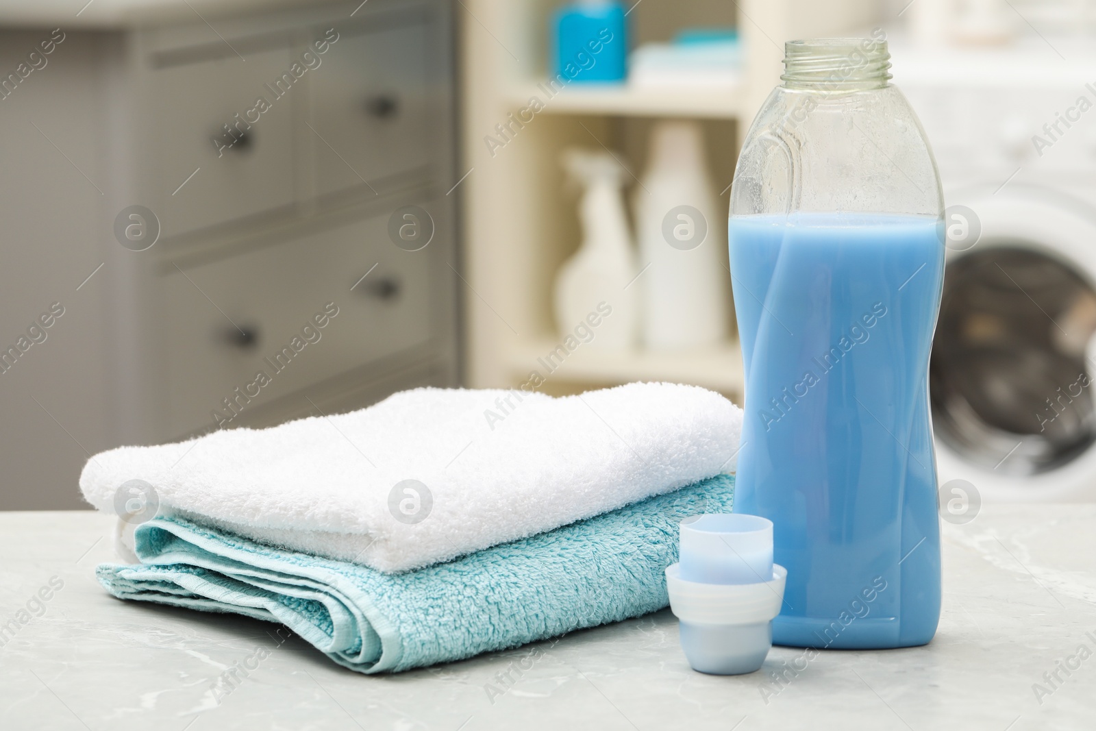 Photo of Laundry detergent and clean terry towels on light grey marble table in bathroom