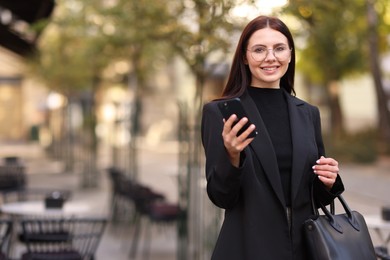 Photo of Smiling businesswoman in stylish suit with smartphone outdoors. Space for text