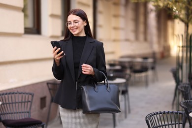 Photo of Smiling businesswoman in stylish suit with smartphone outdoors. Space for text