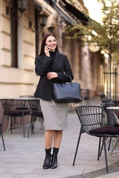 Photo of Smiling businesswoman in stylish suit talking on smartphone outdoors