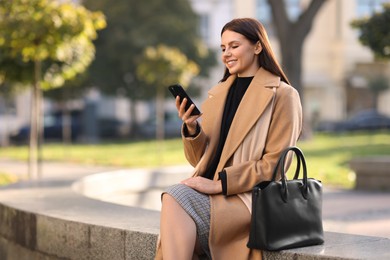 Smiling businesswoman in stylish suit with smartphone outdoors. Space for text