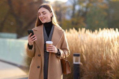 Photo of Smiling businesswoman in stylish suit using smartphone outdoors. Space for text