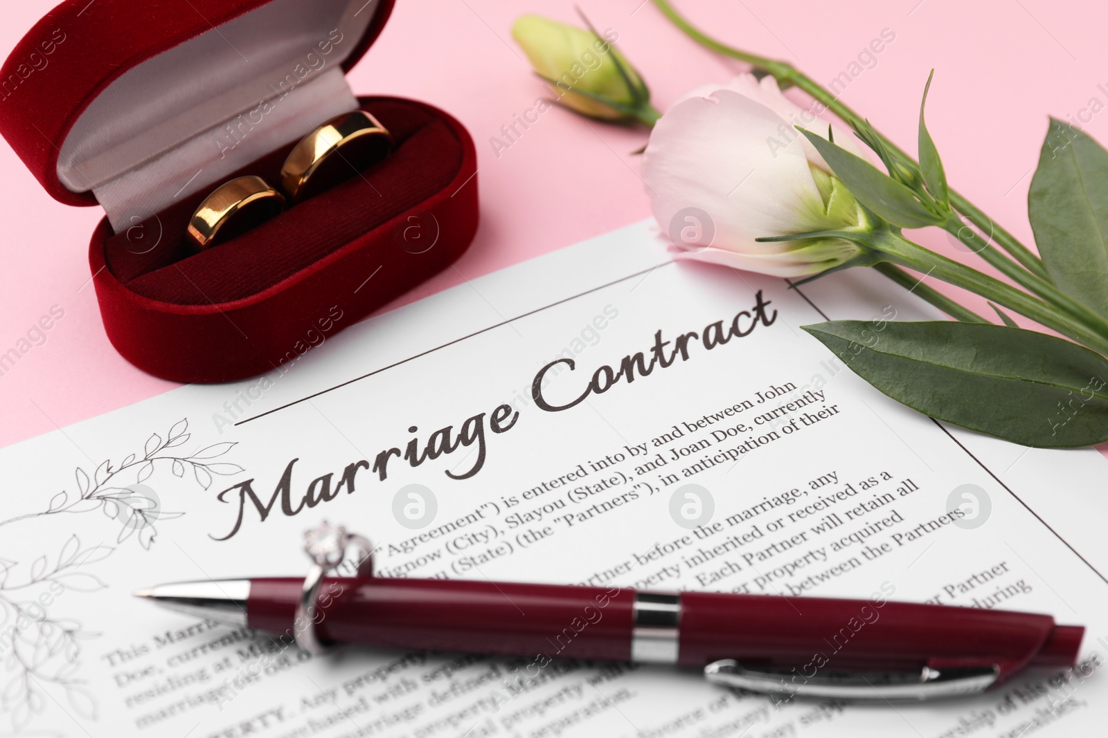 Photo of Marriage contract, pen, flowers and golden rings on pink background, closeup