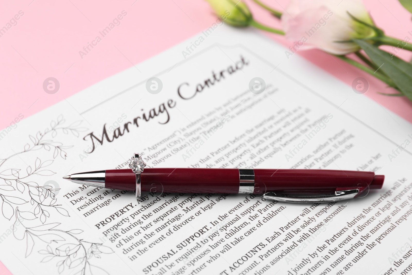 Photo of Marriage contract, pen, flowers and ring on pink background, closeup