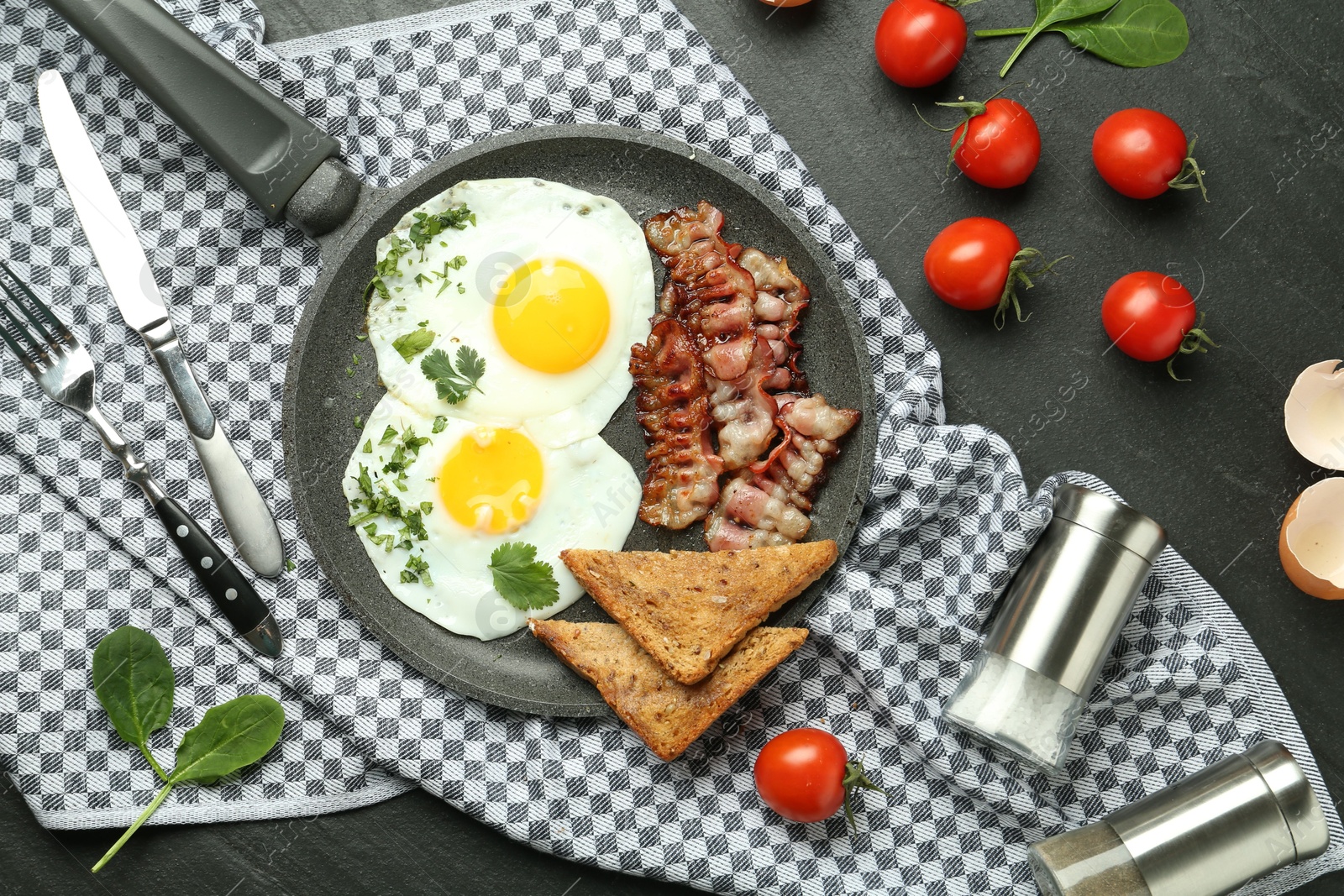 Photo of Tasty fried eggs, bacon and pieces of toast served on black table, flat lay