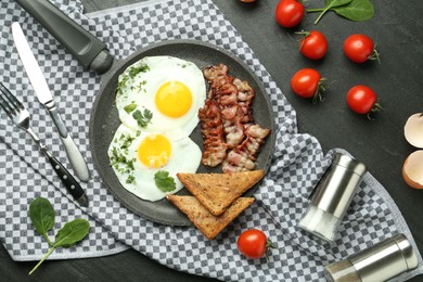 Photo of Tasty fried eggs, bacon and pieces of toast served on black table, flat lay