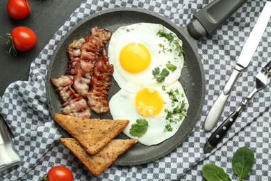 Photo of Tasty fried eggs, bacon and pieces of toast served on black table, flat lay