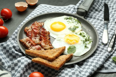 Photo of Tasty fried eggs, bacon and pieces of toast served on black table, closeup