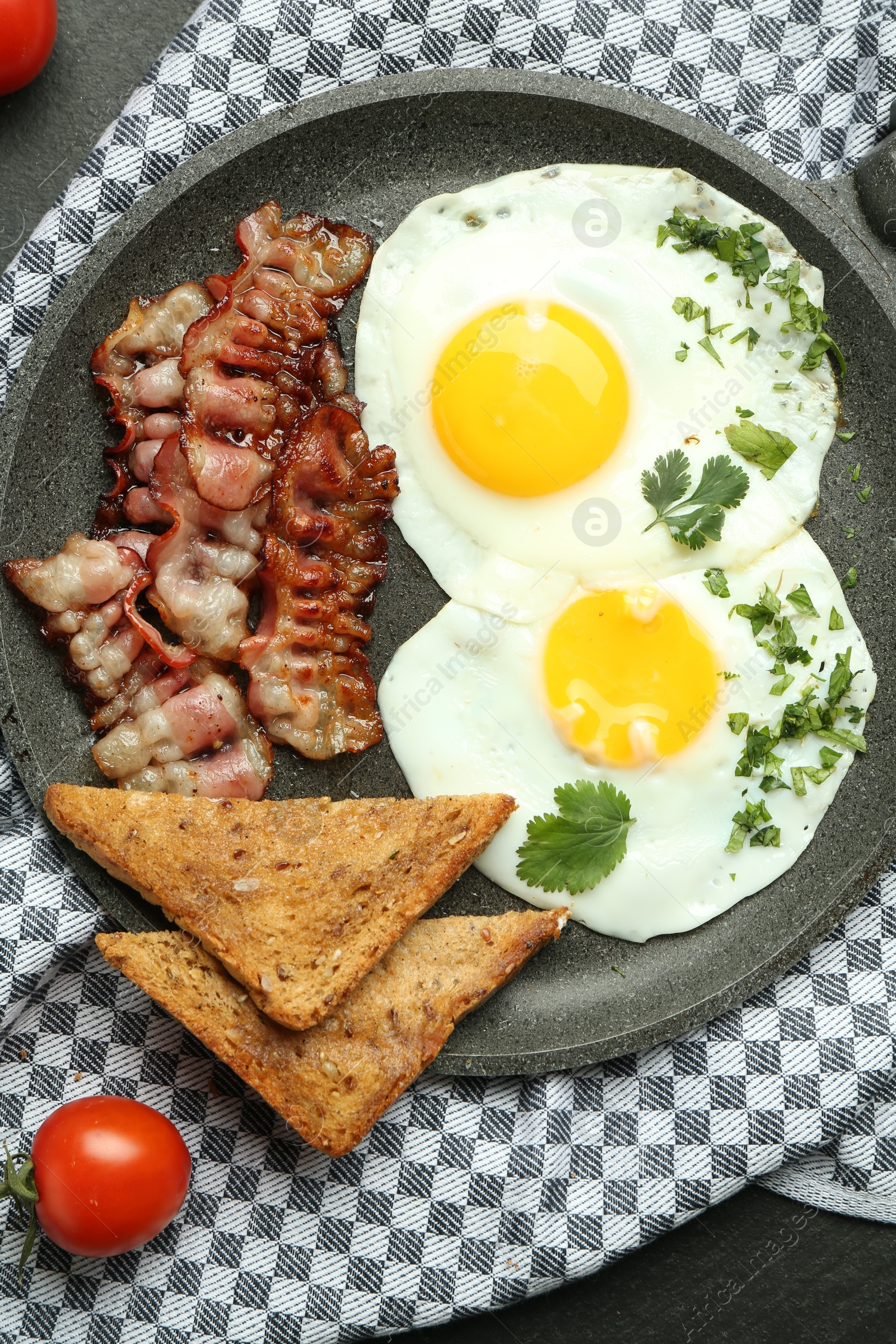 Photo of Tasty fried eggs, bacon and pieces of toast on black table, flat lay