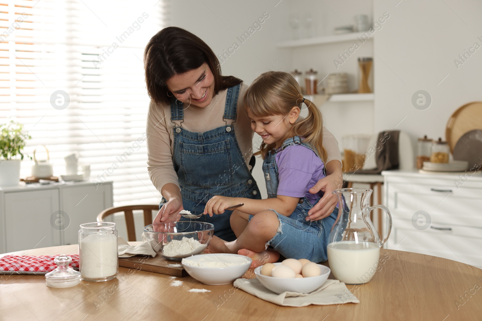 Photo of Little girl helping her mom making dough at table in kitchen