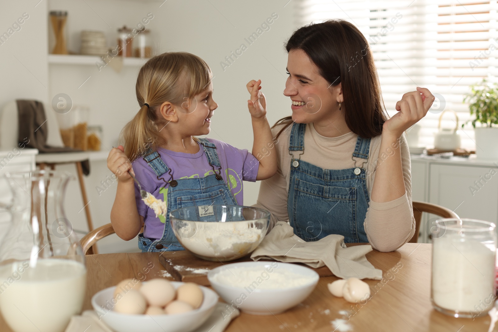 Photo of Little girl helping her mom making dough at table in kitchen