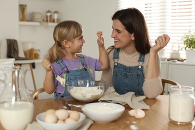 Little girl helping her mom making dough at table in kitchen