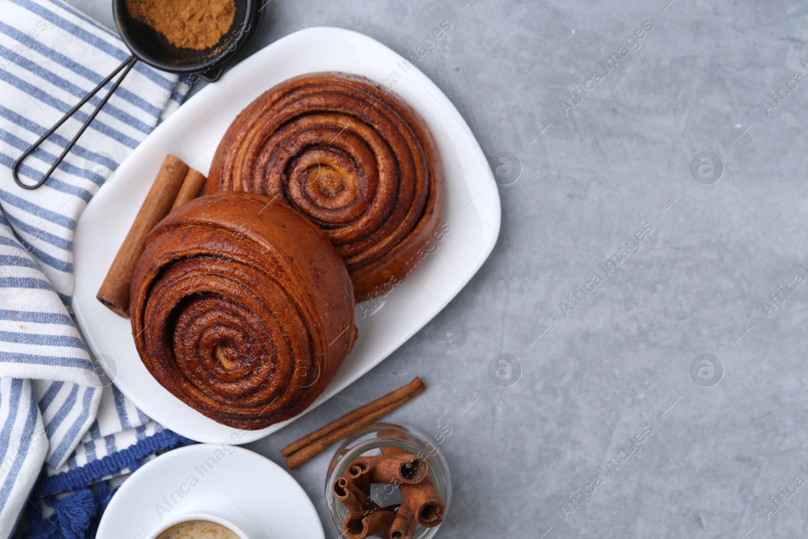 Photo of Delicious cinnamon rolls, sticks and powder on grey textured table, flat lay. Space for text