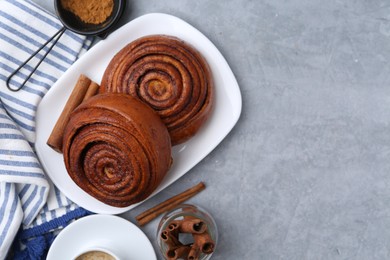 Photo of Delicious cinnamon rolls, sticks and powder on grey textured table, flat lay. Space for text