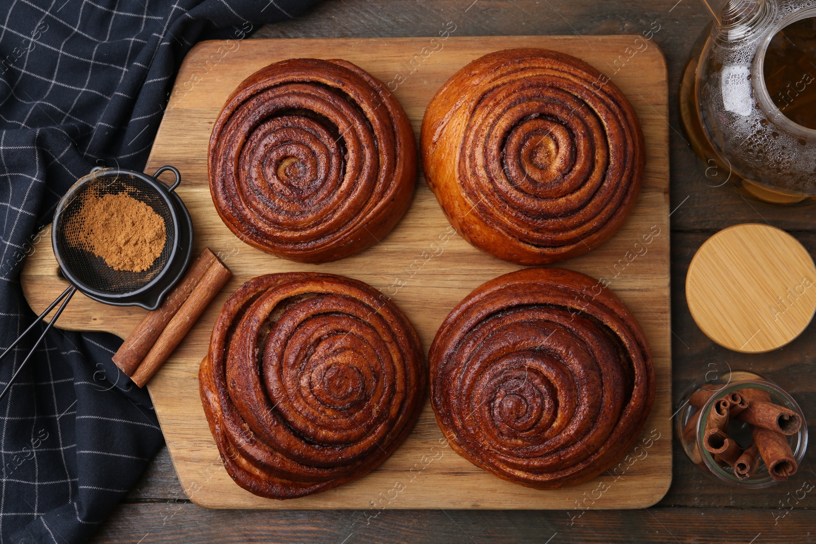 Photo of Delicious cinnamon rolls, sticks and powder on wooden table, flat lay