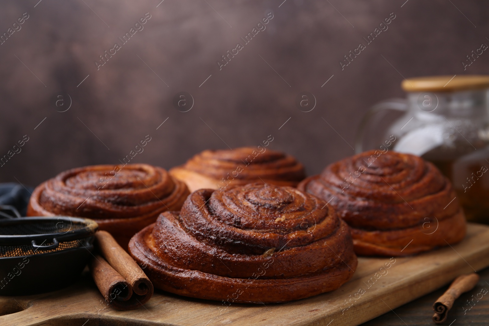 Photo of Delicious cinnamon rolls on wooden table against brown background, closeup