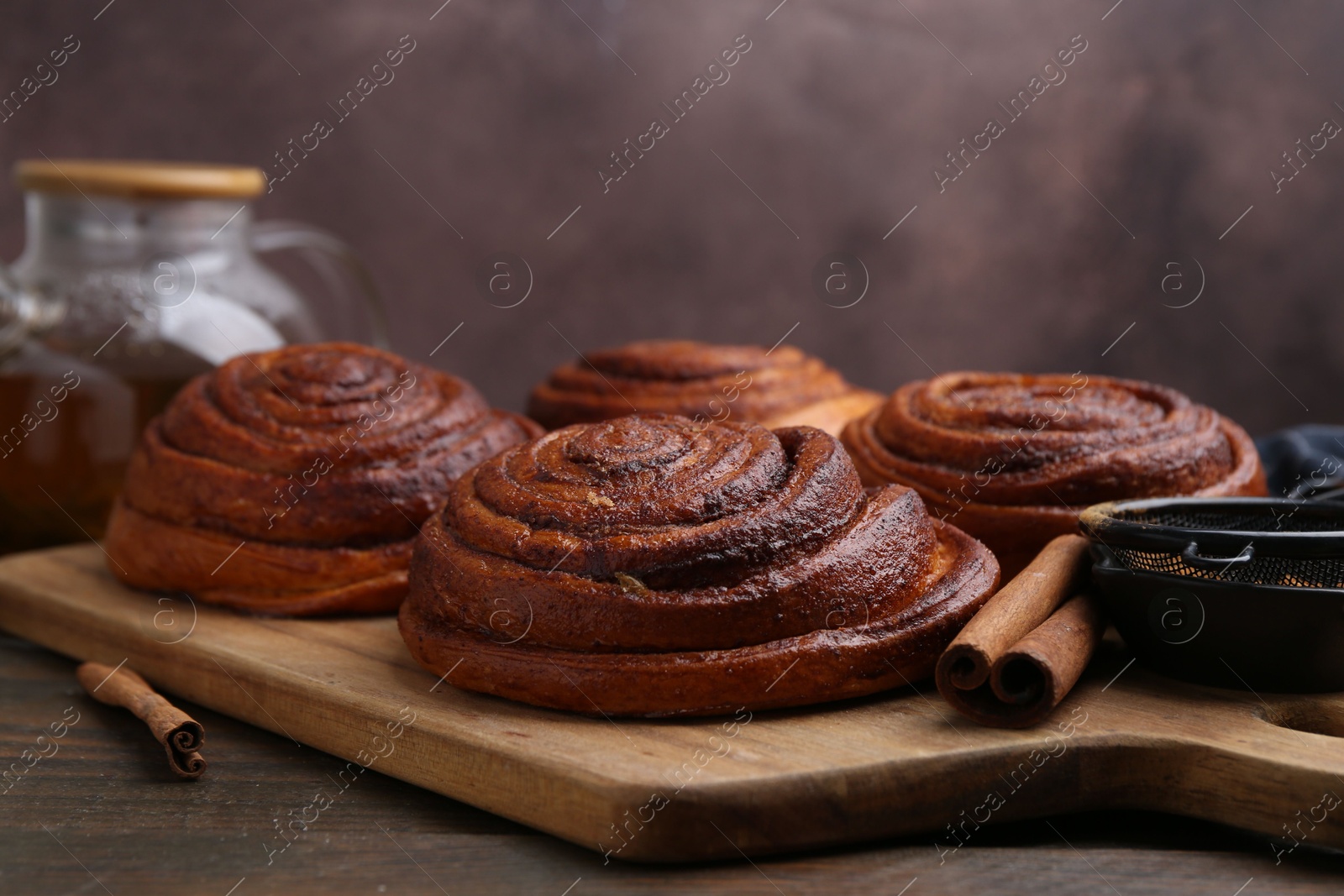 Photo of Delicious cinnamon rolls on wooden table against brown background, closeup