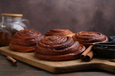 Photo of Delicious cinnamon rolls on wooden table against brown background, closeup