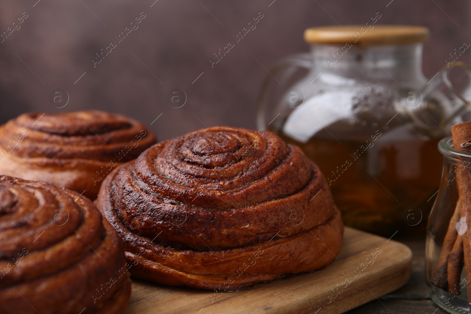 Photo of Delicious cinnamon rolls on wooden table against brown background, closeup