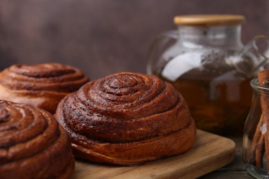 Photo of Delicious cinnamon rolls on wooden table against brown background, closeup