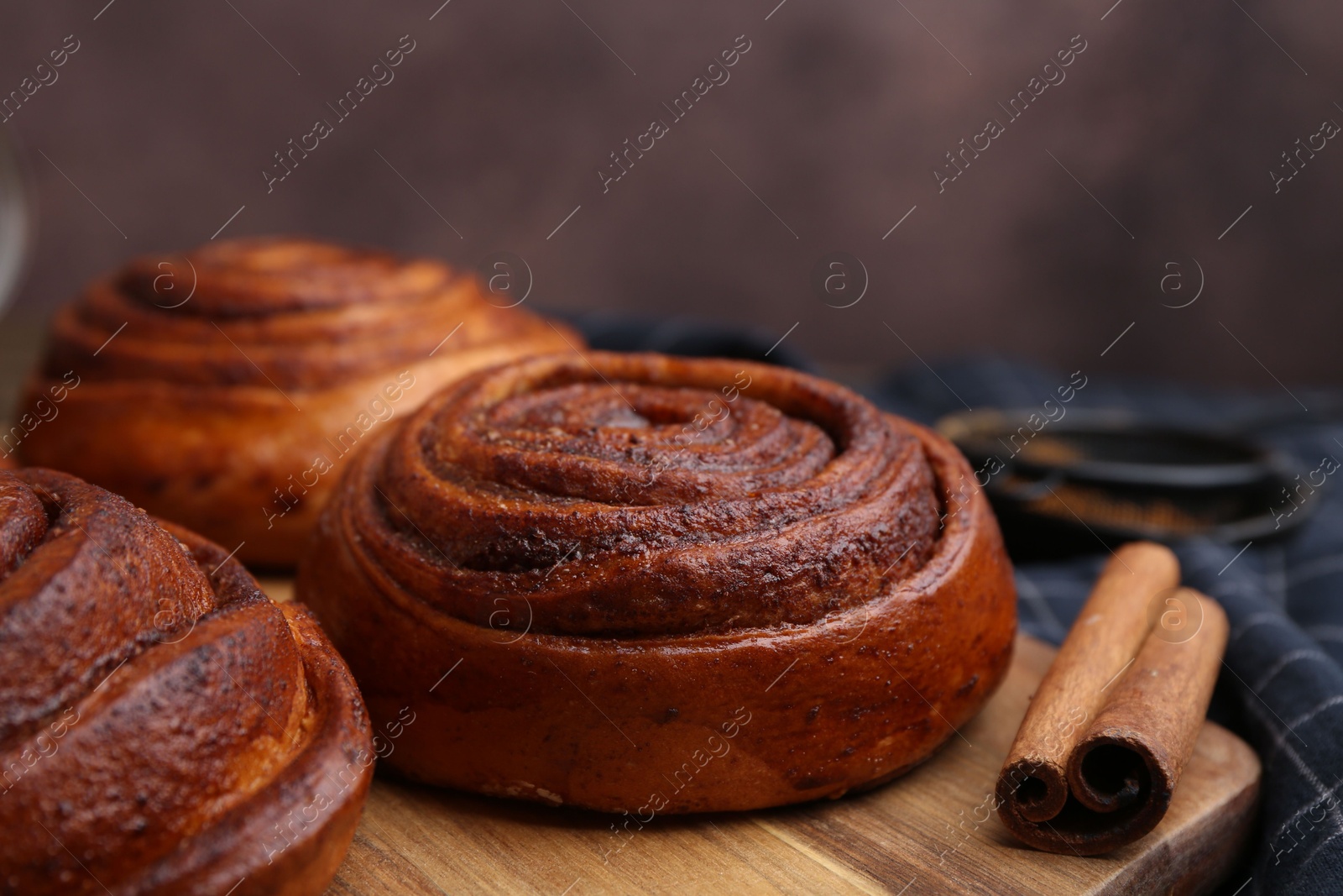 Photo of Delicious cinnamon rolls on table against brown background, closeup