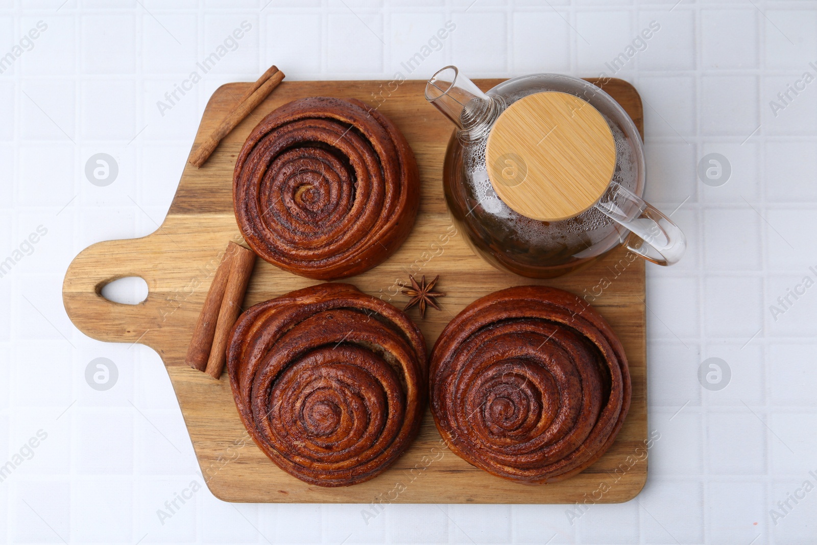 Photo of Delicious cinnamon rolls, tea and spices on white tiled table, top view