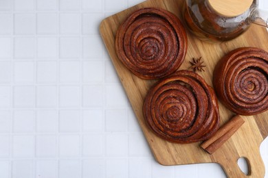 Photo of Delicious cinnamon rolls, tea and spices on white tiled table, top view. Space for text