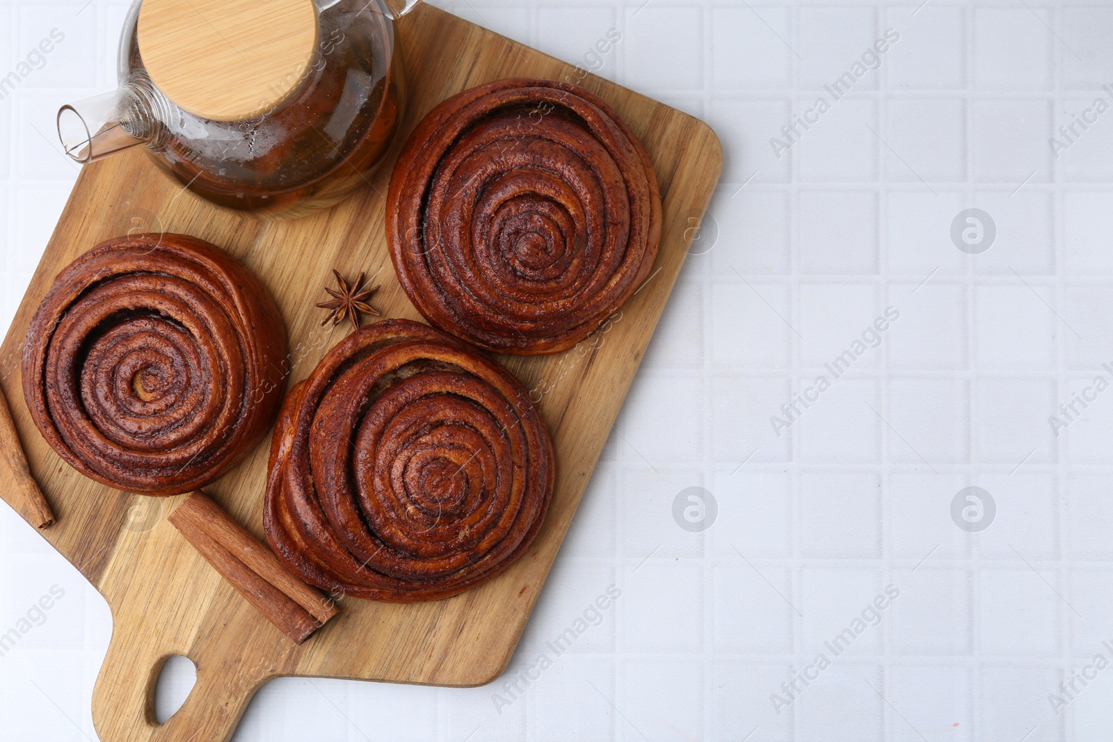 Photo of Delicious cinnamon rolls, tea and spices on white tiled table, top view. Space for text