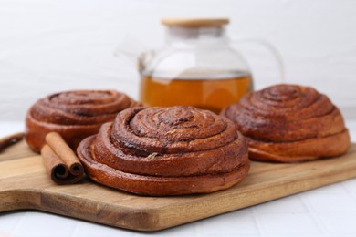 Photo of Delicious cinnamon rolls and stick on white tiled table, closeup