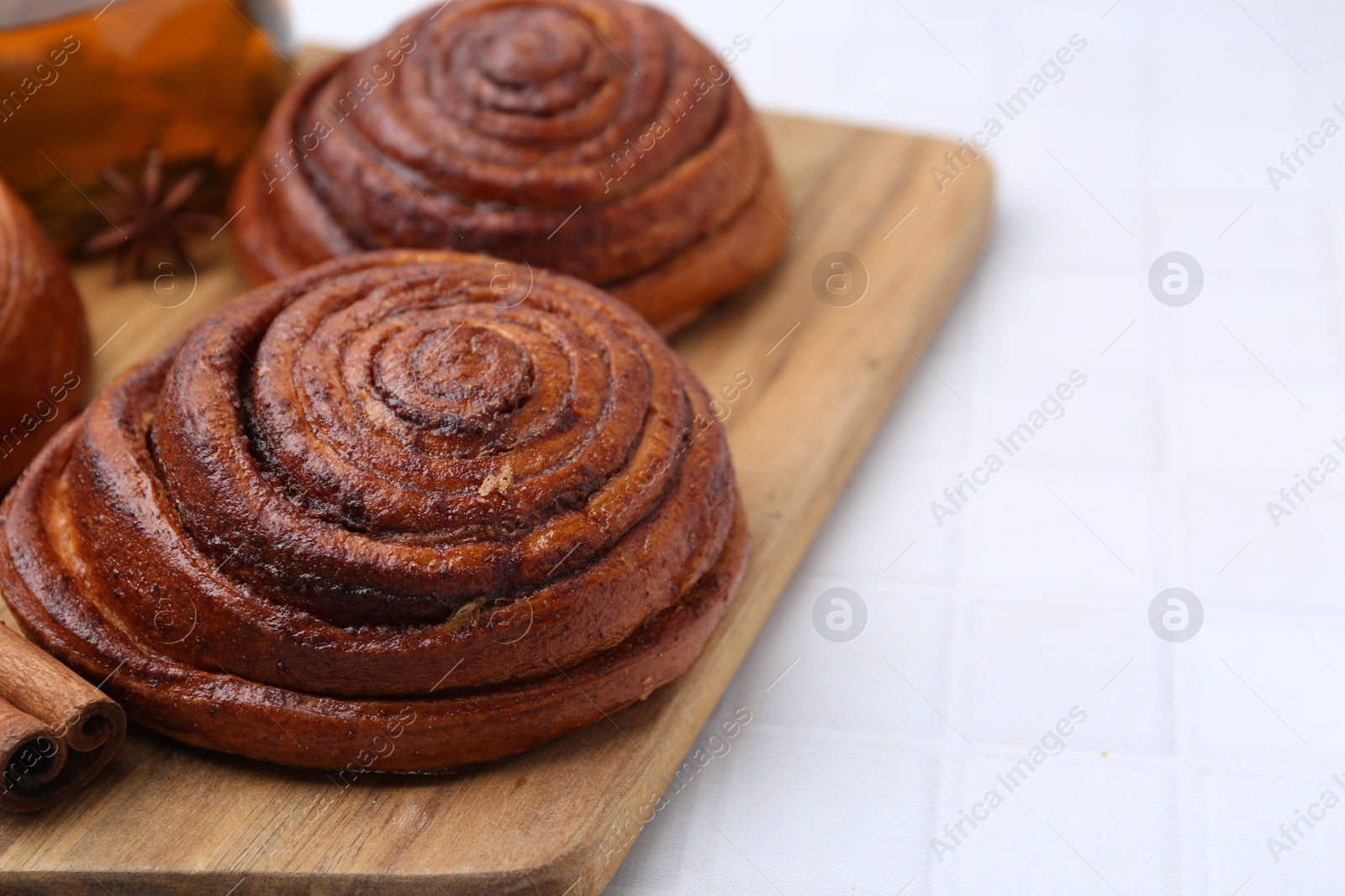 Photo of Delicious cinnamon rolls on white tiled table, closeup. Space for text