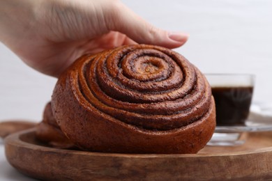 Photo of Woman taking delicious cinnamon roll from board at table, closeup