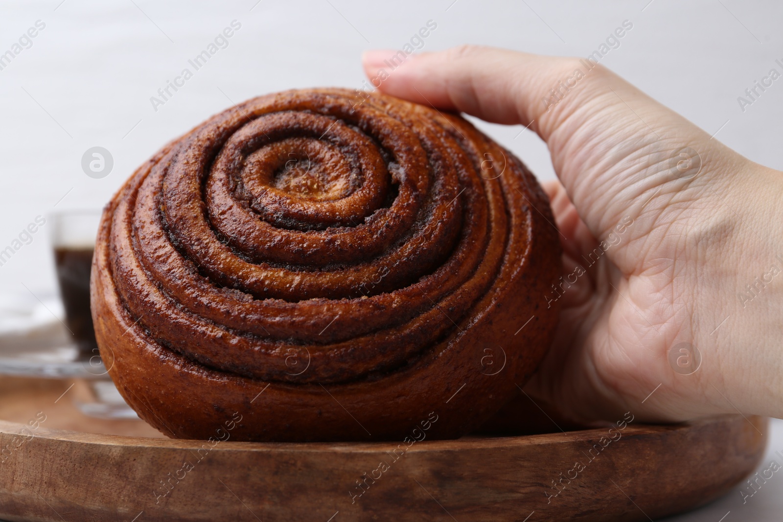 Photo of Woman taking delicious cinnamon roll from board at table, closeup