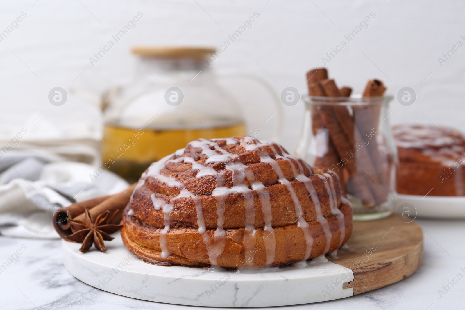 Photo of Tasty cinnamon roll with cream and spices on white marble table, closeup