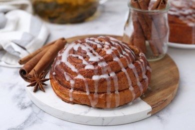 Photo of Tasty cinnamon roll with cream and spices on white marble table, closeup