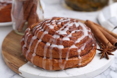 Photo of Tasty cinnamon roll with cream and spices on white marble table, closeup