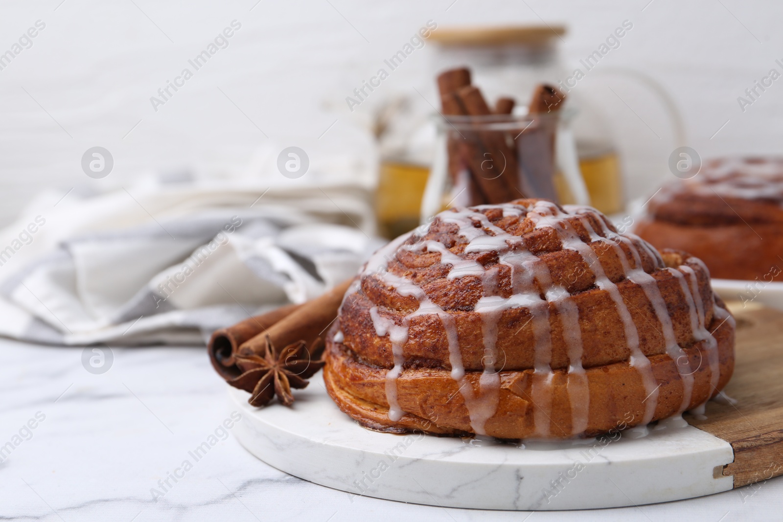 Photo of Tasty cinnamon roll with cream and spices on white marble table, closeup. Space for text