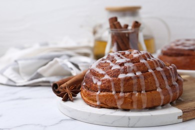 Photo of Tasty cinnamon roll with cream and spices on white marble table, closeup. Space for text