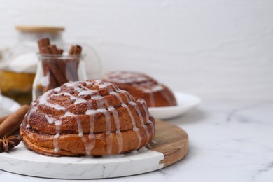 Photo of Tasty cinnamon roll with cream and spices on white marble table, closeup. Space for text