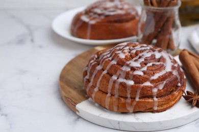 Photo of Tasty cinnamon roll with cream and spices on white marble table, closeup