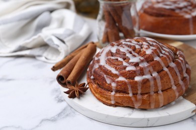 Photo of Tasty cinnamon roll with cream and spices on white marble table, closeup