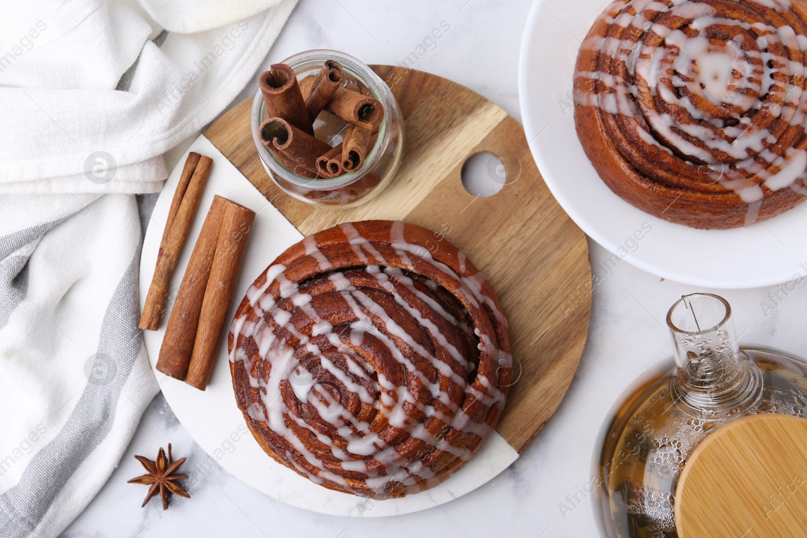 Photo of Tasty cinnamon rolls with cream, spices and tea on white table, flat lay